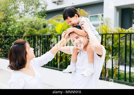 Carino padre asiatici piggybacking suo figlio insieme con sua moglie nel parco. Famiglia entusiasti di trascorrere del tempo insieme con la felicità Foto Stock