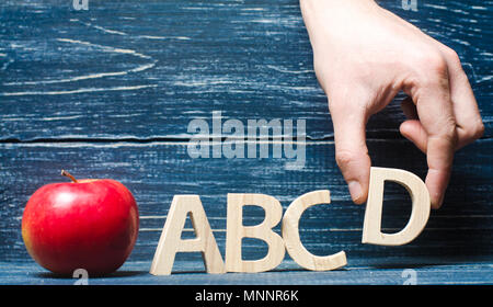 Red apple e lettere ABCD. La mano mette la lettera D in ordine alfabetico. Apple per l'insegnante. Il concetto dell insegnamento e dell educazione. Scuola, co Foto Stock