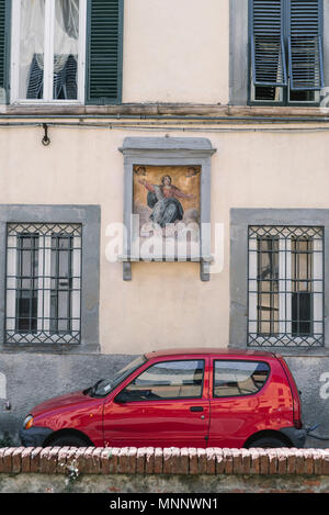 Una piccola auto rossa nella parte anteriore di un vecchio edificio a Lucca, Italia. Foto Stock