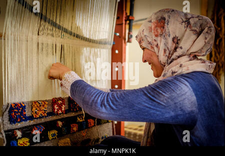 Una donna in abito tradizionale si siede la tessitura dei tappeti in Tazenakht, sud del Marocco, Africa Foto Stock