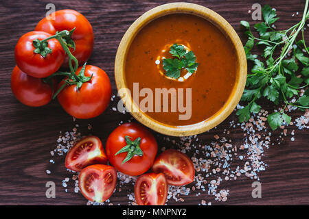 Zuppa di pomodoro in una ciotola di legno con sale di roccia e pomodori organici Foto Stock