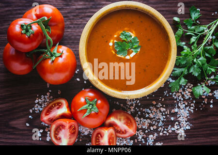 Zuppa di pomodoro in una ciotola di legno con sale di roccia e pomodori organici Foto Stock