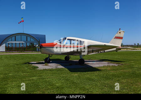 Il piano Piper Cherokee sorge sull'erba verde in una giornata di sole. Una piccola aviosuperficie privata con piani diversi. Aviazione privata Foto Stock