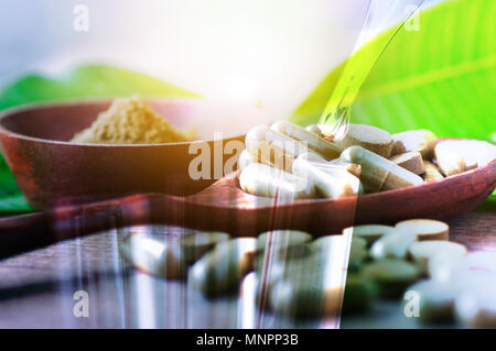 Doppia esposizione tubo di test e farmaci a base di erbe in pillole e capsule sulla tavola di legno con foglie verdi, mixed media Foto Stock