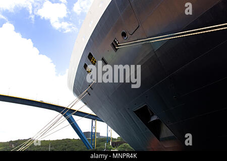 Un enorme contenitore nave o nave da crociera è una cordata di dock accanto a un ponte Foto Stock