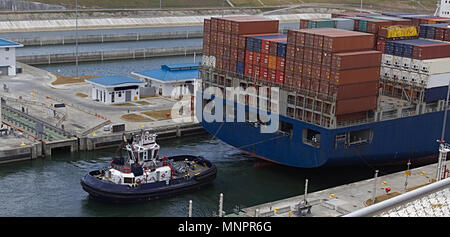 Un rimorchiatore funziona con un enorme nave container in un canale per tirare o spingere attraverso Foto Stock