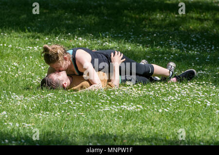 Una giovane coppia abbracciando e baciando la posa sull'erba in uno spazio verde o parco nel centro di una città in una calda giornata d'estate. stare insieme e di amore. Foto Stock