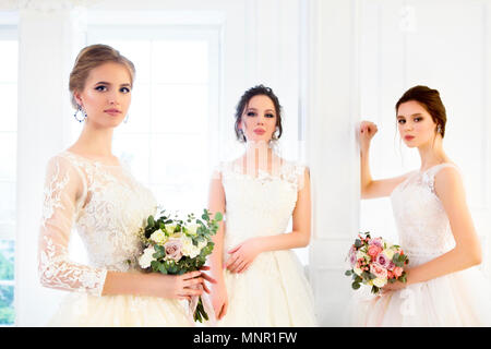 Tre giovane donna con bouquet che indossa abiti da sposa Foto Stock