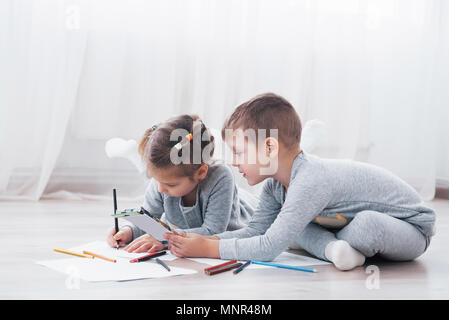 I bambini si trovano sul pavimento in pigiama e disegnare con matite. Carino bambino dipinto di matite Foto Stock