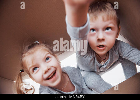 Due un po' i bambini un ragazzo e una ragazza apertura di una scatola di cartone e arrampicate nel mezzo di esso. I bambini si divertono Foto Stock