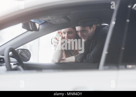 Di acquistare la loro prima vettura insieme. Angolo di Alta Vista del giovane venditore auto in piedi presso la concessionaria dicendo circa le caratteristiche della vettura per i clienti Foto Stock