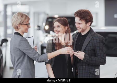 Di acquistare la loro prima vettura insieme. Angolo di Alta Vista del giovane venditore auto in piedi presso la concessionaria dicendo circa le caratteristiche della vettura per i clienti Foto Stock