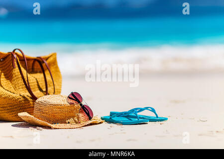 Cappello di paglia, borsa, occhiali da sole e flip flop su una spiaggia tropicale Foto Stock