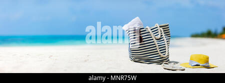 Cappello di paglia, borsa, occhiali da sole e flip flop su una spiaggia tropicale Foto Stock