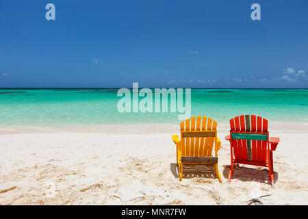 Adirondack colorato di giallo e arancione sedie a sdraio in spiaggia tropicale nei Caraibi con bellissimo oceano turchese acqua, sabbia bianca e blu cielo Foto Stock