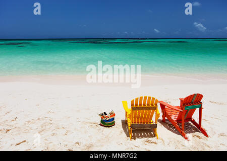 Adirondack colorato di giallo e arancione sedie a sdraio in spiaggia tropicale nei Caraibi con bellissimo oceano turchese acqua, sabbia bianca e blu cielo Foto Stock