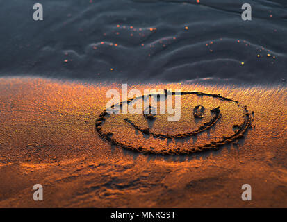 Felice volto sorridente nella sabbia. Gli occhi e la bocca disegnata con un dito asciutto ocherous sabbia. Foto macro close up dal di sopra. Foto Stock