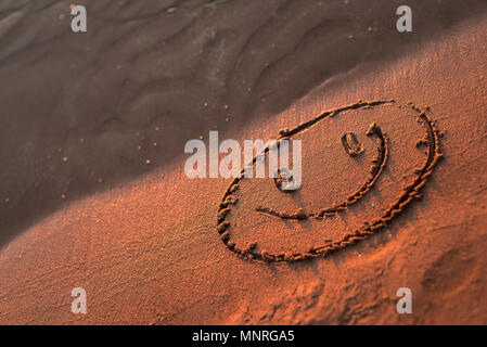 Felice volto sorridente nella sabbia. Gli occhi e la bocca disegnata con un dito asciutto ocherous sabbia. Foto macro close up dal di sopra. Foto Stock