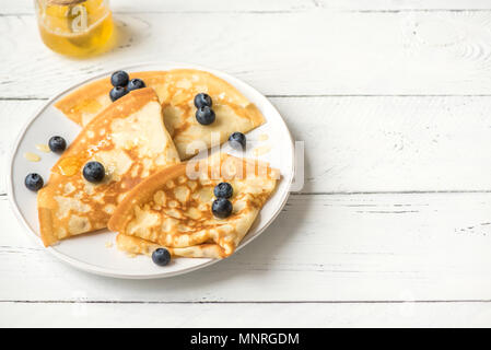 Crepes con mirtilli e miele. Frittelle fatte in casa, crepes sul tavolo bianco, copia dello spazio. Foto Stock