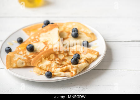 Crepes con mirtilli e miele. Frittelle fatte in casa, crepes sul tavolo bianco, copia dello spazio. Foto Stock