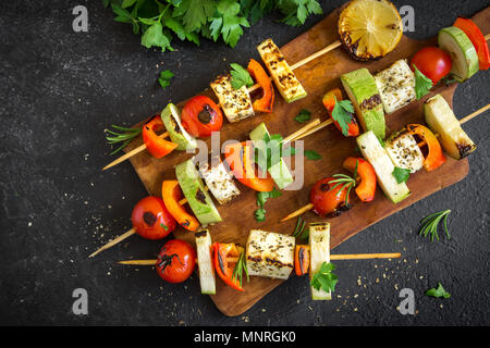 Grill vegetariano. Spiedini vegetariani con il formaggio halloumi e verdure su sfondo nero, copia dello spazio. Foto Stock