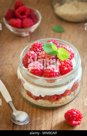 Lampone cheesecake in un barattolo di vetro con lamponi freschi e crema di formaggio su sfondo di legno. Una sana in casa estate berry layered dessert. Foto Stock