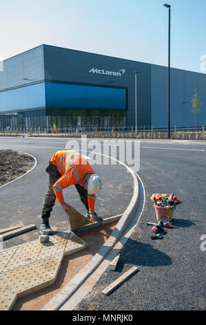 Operaio edile che posa pavimentazione tattile vicino all'edificio del gruppo McLaren, Woking, Regno Unito, in una giornata luminosa. L'industria moderna incontra le infrastrutture pubbliche Foto Stock