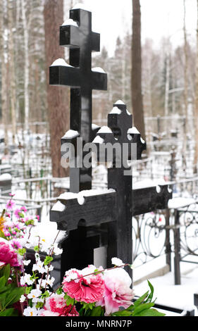 Croci nere e fiori artificiali sulla tomba di un cimitero di ortodossi in inverno Foto Stock