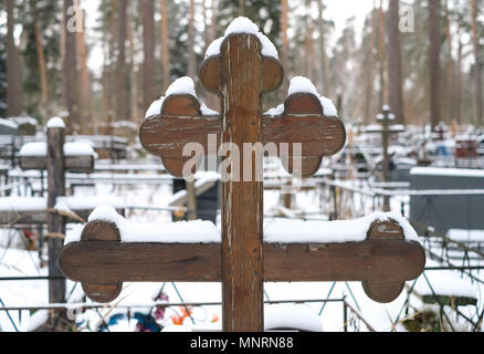 Bella croce di legno di forma tradizionale e fiori artificiali sulla tomba del cimitero di ortodossi in inverno Foto Stock