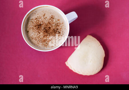 La colazione del mattino con сappuccino. Tazza di caffè con schiuma di latte e cannella o polvere di cacao e bun su rosa luminoso dello sfondo. Foto Stock