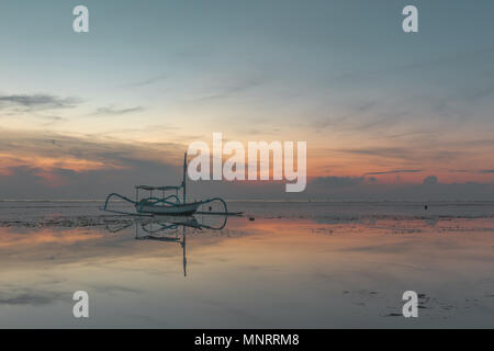 Un indonesiano barca da pesca di sunrise, riflessi nell'acqua, Sanur, Bali, Indonesia, 21 aprile 2018 Foto Stock