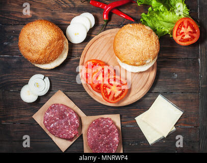 In casa hamburger ingredienti. Materie le carni bovine macinate, fresche bun, fetta di formaggio, pomodoro, cipolla e lattuga su uno sfondo di legno. Foto Stock