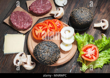 In casa hamburger ingredienti. Materie le carni bovine macinate, fresche black bun, fetta di formaggio, pomodoro, cipolla e lattuga su uno sfondo di legno. Foto Stock