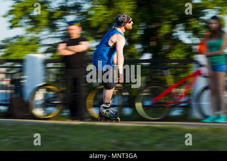 Uomo a cavallo su pattini a rotelle nella città di ciclisti sullo sfondo, illuminate dalla luce del sole Foto Stock