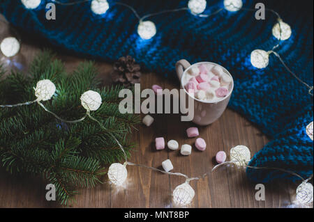 Accogliente casa d'inverno. Tazza di cacao con marshmallows, blu felpa lavorata a maglia, rametto di albero di Natale, garland, fiocchi di neve su un bianco tavolo di legno. Atmosphe Foto Stock