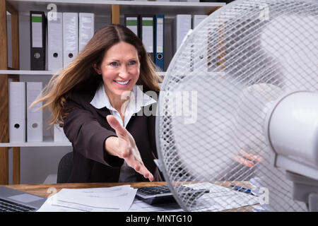 Felice coppia imprenditrice stessa di raffreddamento con ventola elettrica al lavoro Foto Stock