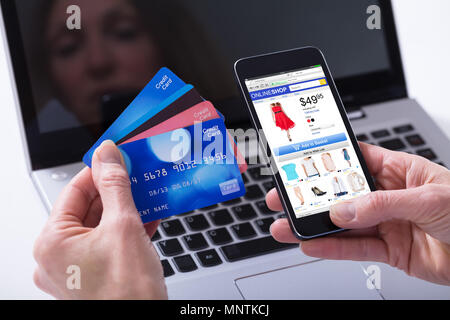 Close-up di una donna shopping online con carte di credito sul proprio telefono cellulare contro il computer portatile Foto Stock