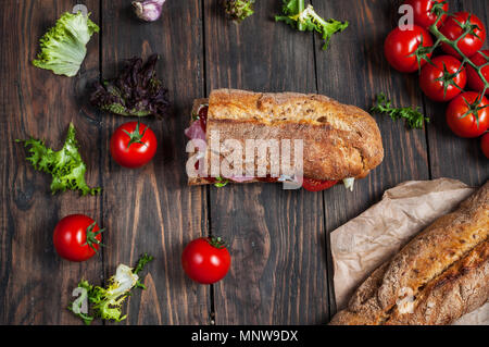 La ciabatta in sandwich con prosciutto, pomodori ciliegini e insalata su sfondo scuro. Foto Stock