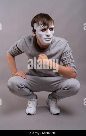 Giovane uomo bello indossare maschera bianca contro lo sfondo grigio Foto Stock