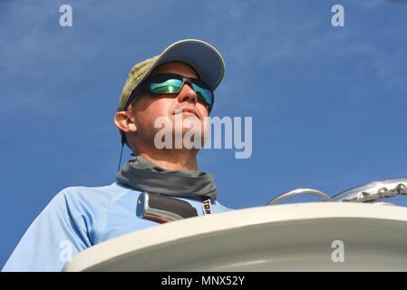 Capitano al volante della barca da pesca, riflettente che indossa gli occhiali  da sole e cappello. La riflessione di acqua e bridge visto in bicchieri,  Orange Beach, Alabama, Stati Uniti d'America Foto stock - Alamy
