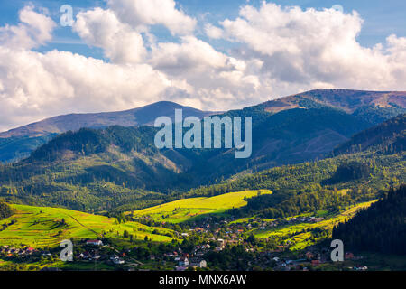 Bellissimo paesaggio urbano in montagna. villaggio ai piedi della montagna. interessante formazione cloud oltre la cresta. erboso campi rurali sulle colline. Foto Stock