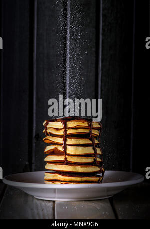 Fresche e deliziose frittelle dolci con zucchero in caduta sulla parte superiore e lo sciroppo al cioccolato salsa Foto Stock