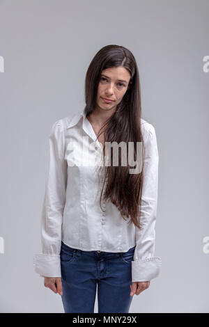 Ritratto di giovane con i capelli lunghi brunette immotivato di letargo donna in piedi contro sfondo semplice Foto Stock