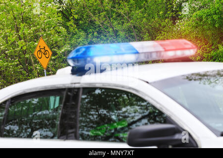 Noleggio bici o cartello stradale con il fuoco selettivo & auto della polizia con sirena attivata luci nel piano sfocato. Una pattuglia di polizia sorveglia la strada. Foto Stock