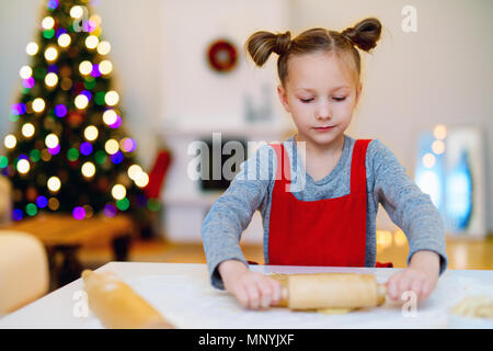 Bambina la cottura biscotti di Natale a casa con la vigilia di Natale. Camere splendidamente arredate, caminetto, albero di Natale e le luci sul background. Foto Stock