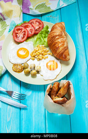 La colazione su un tavolo di legno. Uova fritte, pomodori, brioche Foto Stock