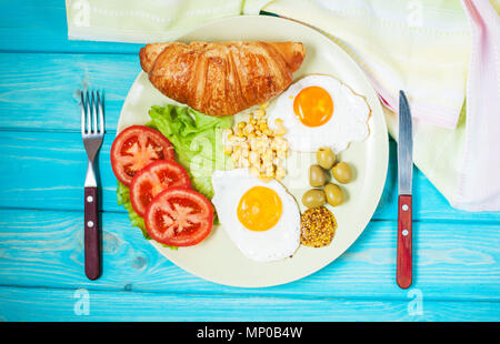 La colazione su un tavolo di legno. Uova fritte, pomodori, croissant. Foto Stock