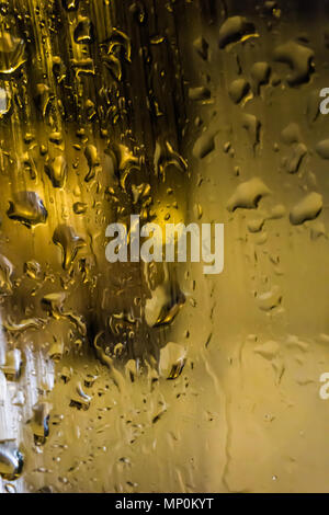 Acqua delle gocce di pioggia su una lastra di vetro in una notte piovosa. Tono di allarme giallo Foto Stock