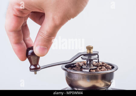 Maschio di macinazione a mano i chicchi di caffè retrò vecchio mulino di caffè isolato su sfondo bianco. Close up, il fuoco selettivo Foto Stock
