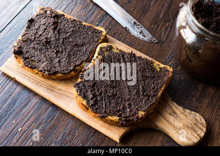 Nero oliva Tapenade su pane con coltello e Jar. Alimenti biologici. Foto Stock